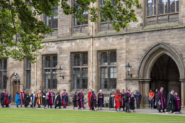 Students in graduation gowns walking outside a large building