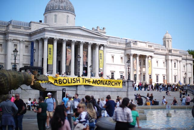 A yellow and black banner bearing the words 'abolish the monarchy' hangs in Trafalgar Square