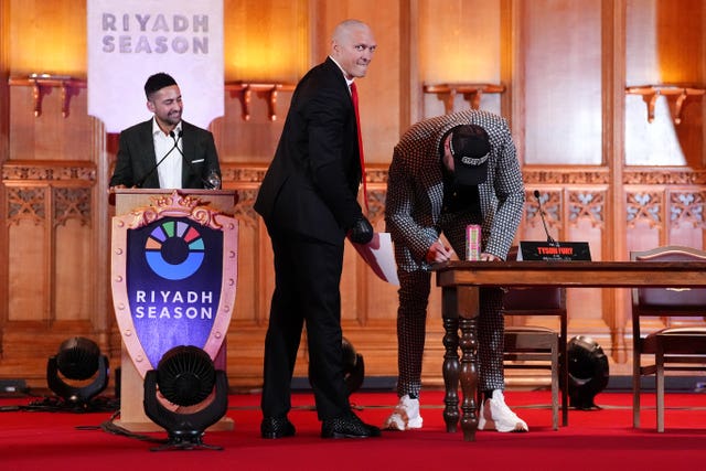 Tyson Fury (right) signs a photo of his previous fight with Oleksandr Usyk (centre left)