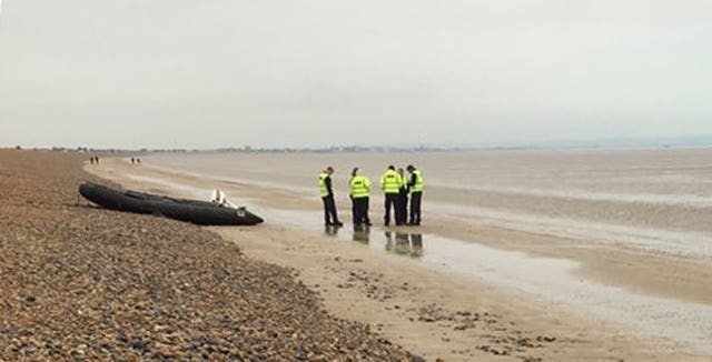 Border Force agents by a empty dinghy on the beach at Lydd-on-Sea