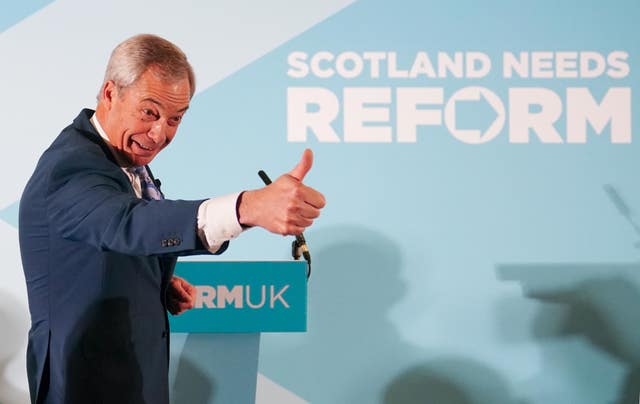 Reform UK leader Nigel Farage on stage holding a thumbs-up