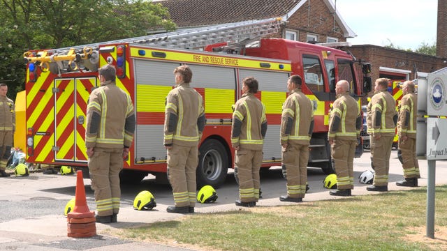 Firefighters in uniform stand in a line as a fire engine drives past them