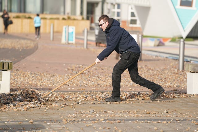 A man uses a broom to sweep pebbles back onto the beach in Brighton