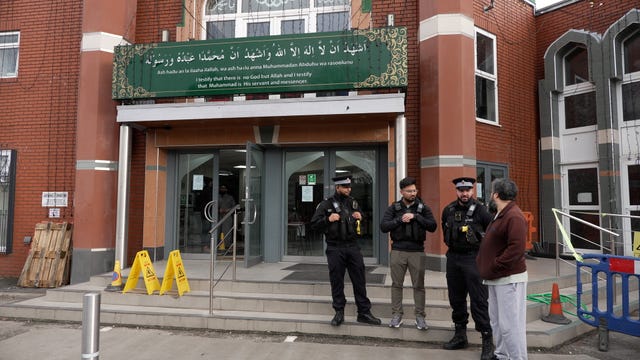 Police officers chat with a man on the steps at the entrance to Manchester Central Mosque