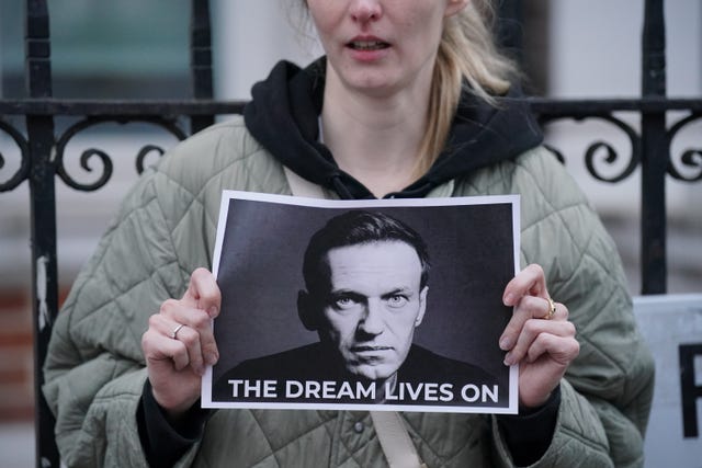 A woman holding a black and white photo of Alexei Navalny, with writing underneath which reads 'The dream lives on'