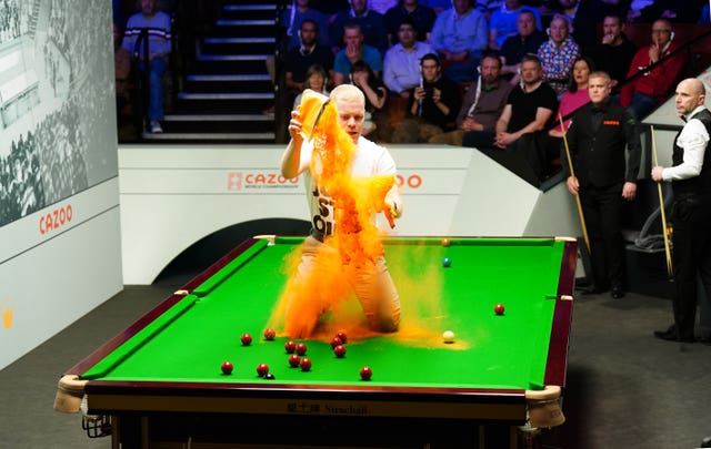 A 'Just Stop Oil' protester jumps on the table and throws orange powder during the match between Robert Milkins and Joe Perry