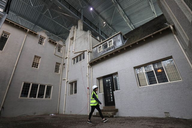 A woman wearing a hard hat and hi-vis vest walks past a door to enter the Hill House