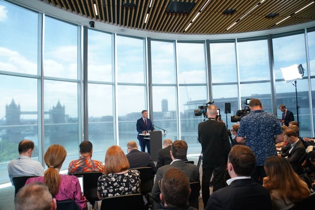Wes Streeting speaking from a podium in the distance in front of members of the media in the foreground