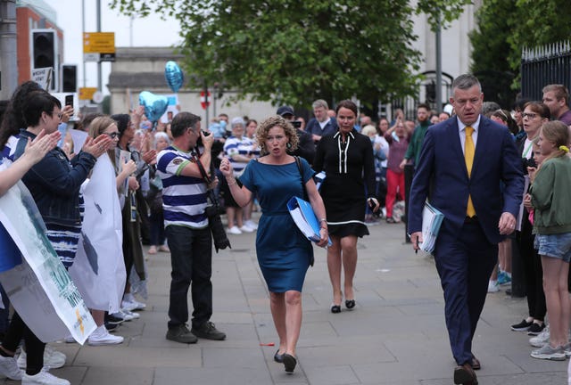 Fiona Donohoe with one hand raised and carrying a folder, walking past scores of supporters