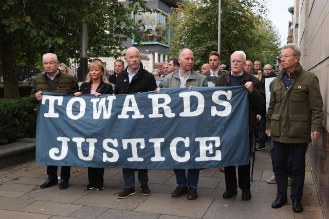 The brothers of Bloody Sunday victim William McKinney, Mickey (left), John (centre) and Joe (right) at Belfast Crown Court holding a banner reading Towards Justice