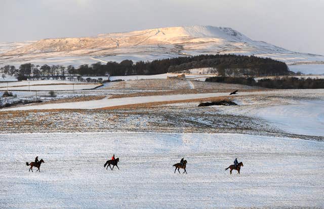 The Pennine hilltops are covered with snow as riders make their way onto the gallops at Middleham Moor near Leyburn (John Giles/PA)