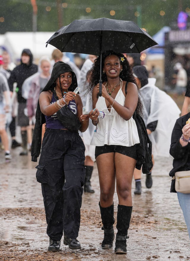 Festivalgoers shelter from the rain as they walk through the muddy site at the Reading Festival at Little John’s Farm, Reading, Berkshire.