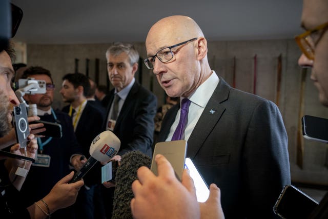 John Swinney speaking while surrounded by reporters