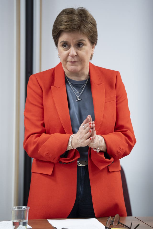 Nicola Sturgeon standing while at a desk, with her hands clasped together