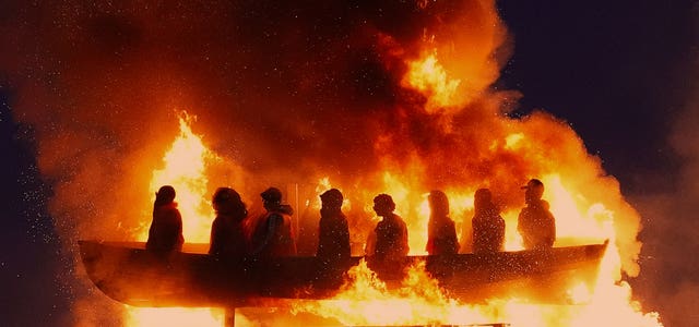Effigies of migrants in a boat burning on a bonfire