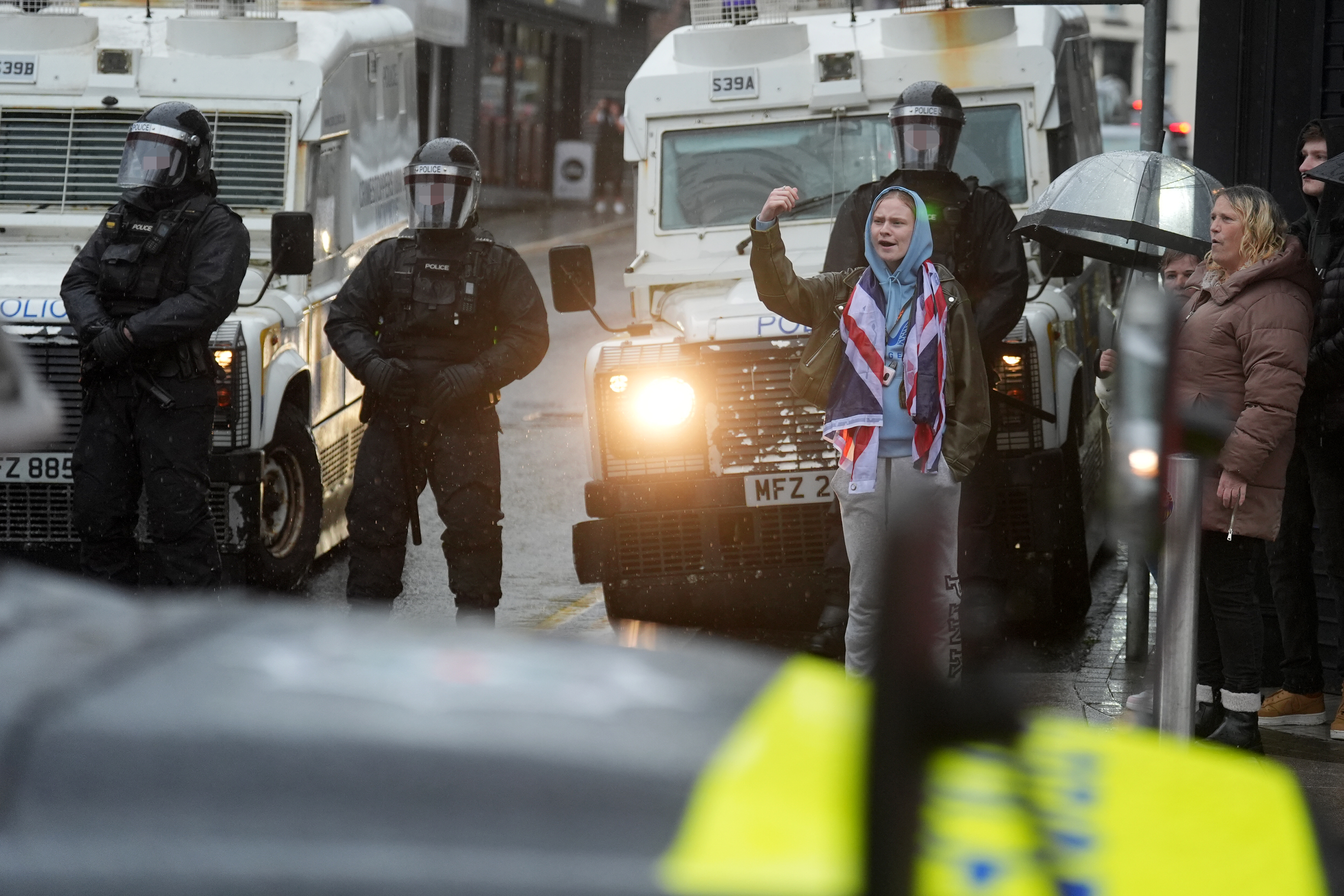 A person wearing a Union flag stands near armed police