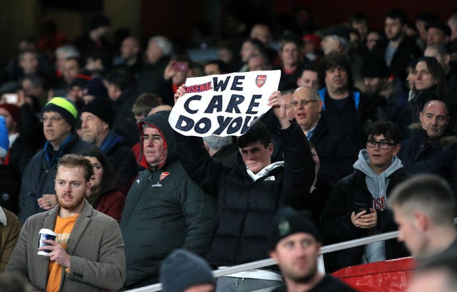 An Arsenal fan holds up a 'We care, do you?' banner