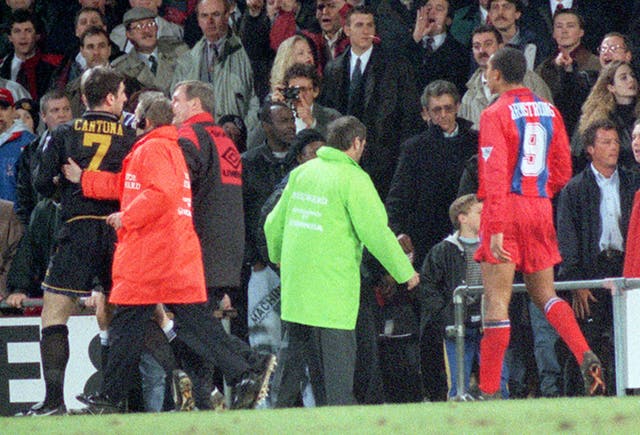 Cantona is escorted off the pitch after lunging at a fan in the crowd at Selhurst Park