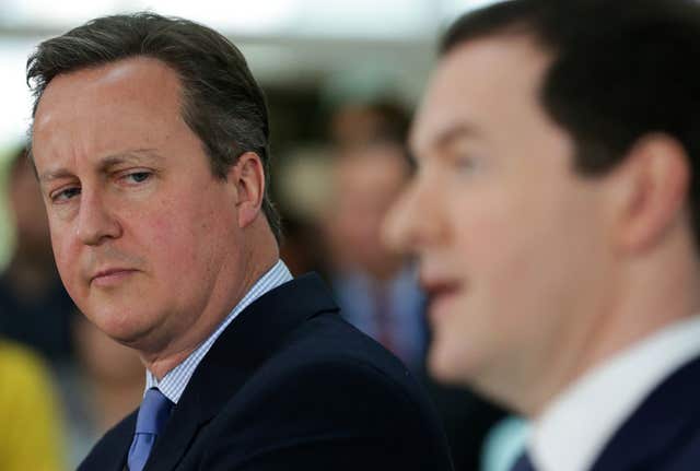 Side view of George Osborne speaking, while David Cameron looks at him