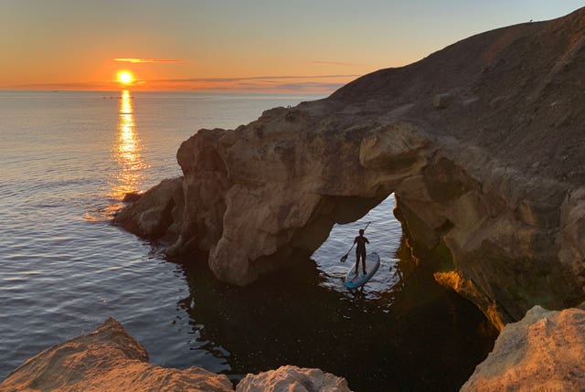 A paddleboarder watches the sun rise at Cullercoats bay in North Tyneside on August 8