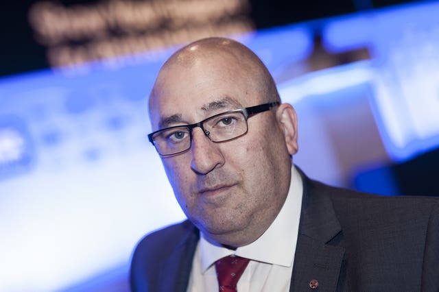 A head and shoulders shot of the head of the Metropolitan Police Federation, Ken Marsh, wearing a suit and tie, and glasses, standing in front of a blurred background.