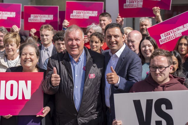 Anas Sarwar and Davy Russell smiling and giving the thumbs-up, surrounded by Labour supporters holding placards