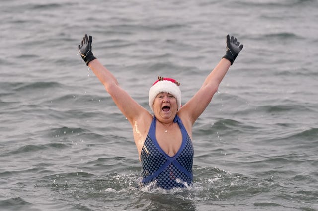 A woman in the sea raises her arms above her head