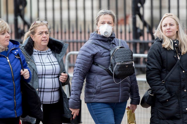 A woman wearing a protective face mask walks past Buckingham Palace