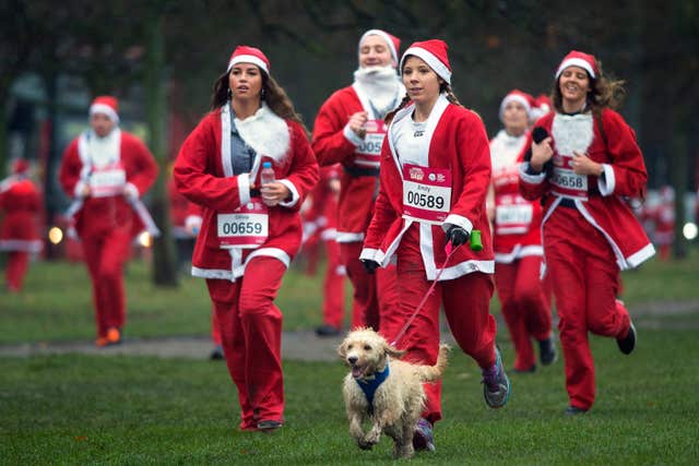 People dressed as Santa Claus run with a dog during the Santa Dash