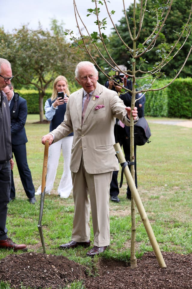 The King holds a tree after a tree planting ceremony during a visit to the National Stud in Newmarket, Suffolk