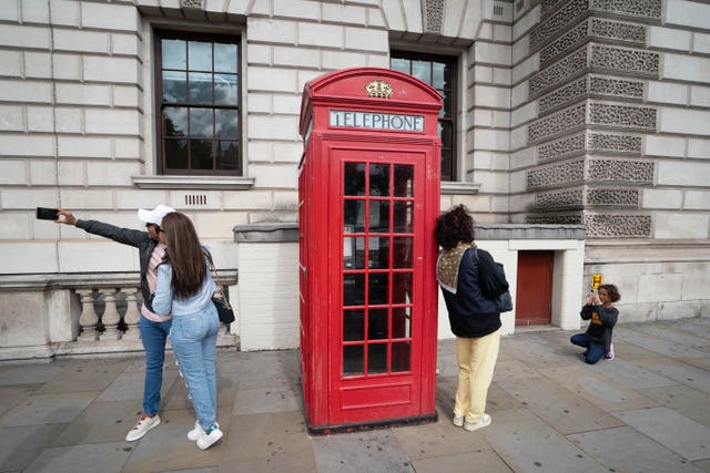 Tourists to London have their photo taken beside a red phone box at Parliament Square