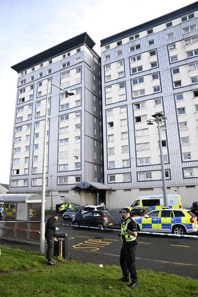 Police officers in the foreground, in front of a tower block which has several police vehicles parked outside