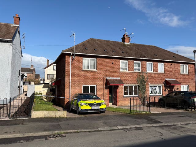 An end terrace house which has a police car parked in the driveway, and police tape cordoning off the area