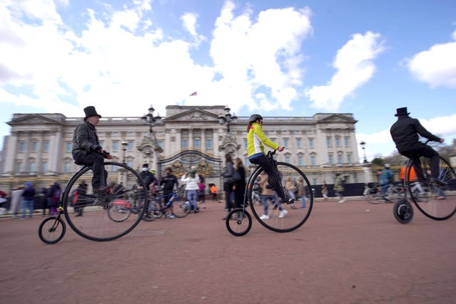 People ride penny farthings past Buckingham Palace