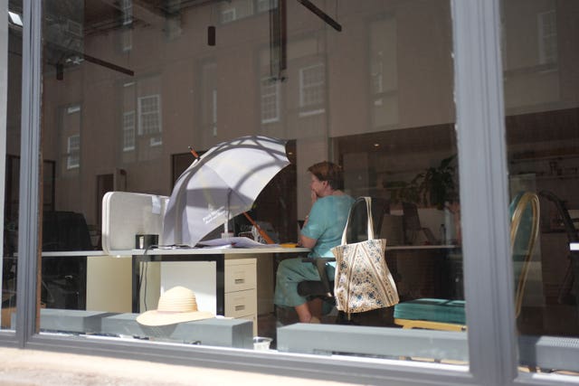 An office worker uses an umbrella to shade her workspace from the sun in Westminster, central London