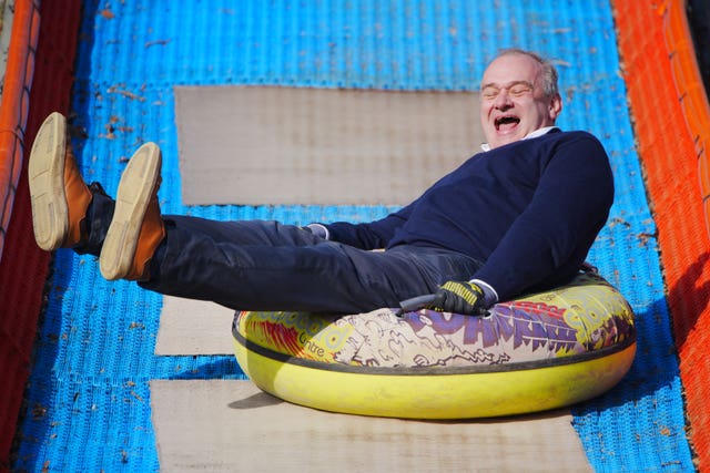 Sir Ed Davey laughing while travelling down a slide on an inflatable