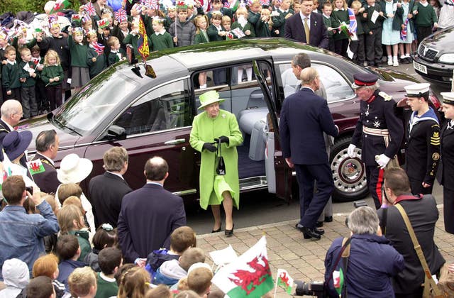 The late Queen in a lime green outfit steps from her Bentley state limousine as a crowd and guards look on