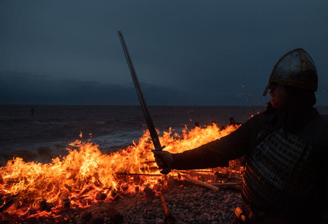 A re-enactor looks on as a longboat burns