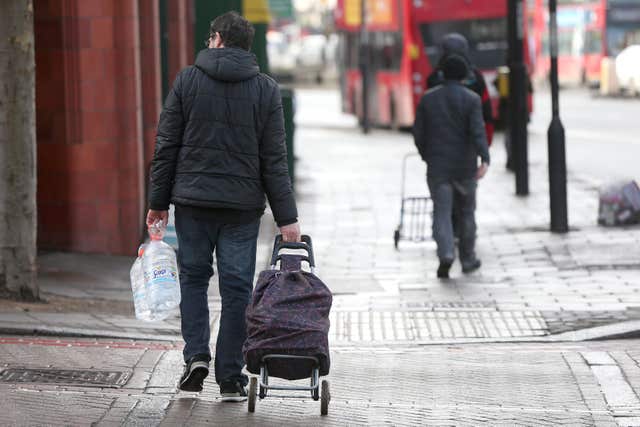 A shopper carries large bottles of water along Streatham Hill in London (Jonathan Brady/PA)