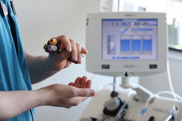 A donor carer holds vials of blood in front of an apheresis machine which separates plasma from blood as people donate blood plasma for medicine