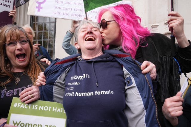 Women celebrating, one with pink hair and another wearing a T-shirt which reads 'Woman - adult human female'