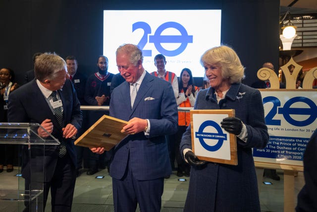 The Prince of Wales and Duchess of Cornwall holding commemorative plaques during a visit to the London Transport Museum to mark 20 years of Transport for London