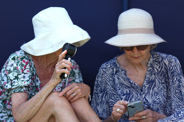 Two women wearing sun hats, with one using a handheld electric fan to keep cool