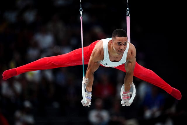 Joe Fraser, dressed in red bottoms and a white vest, on the gymnastic rings.