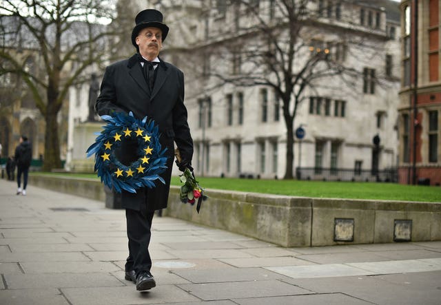 A man dressed as an undertaker holding a wreath with an EU flag