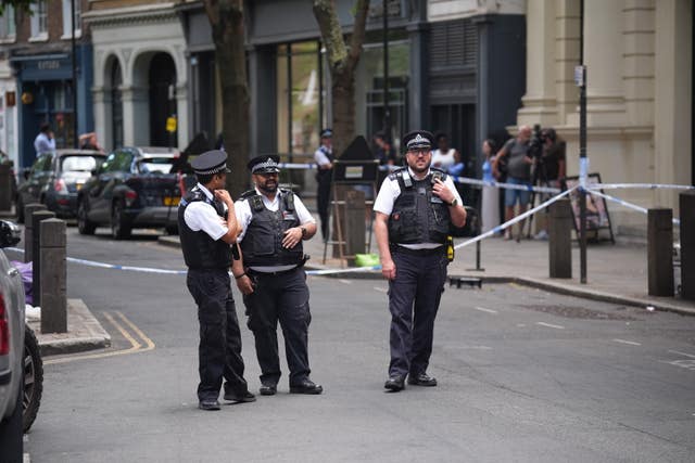Three police officers standing on a road within a tapped off cordon