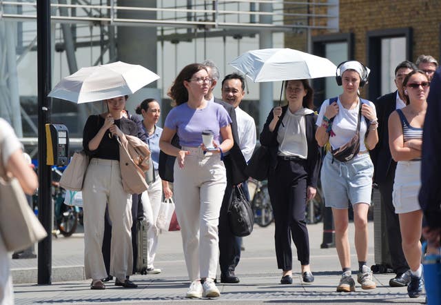 Commuters walking outside, some using umbrellas for shade
