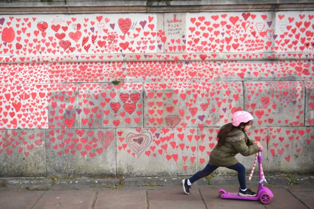 A young girl rides a scooter past the National Covid Memorial Wall