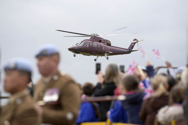 A royal helicopter carrying the King flies above a crowd as it prepares to land