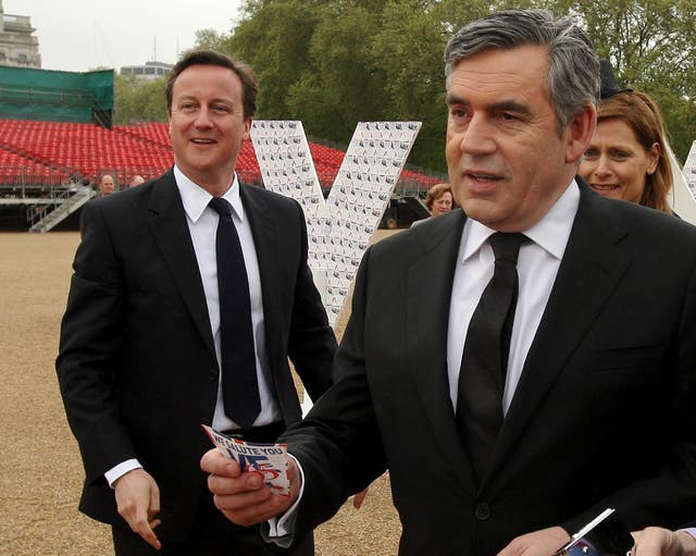 Prime Minister Gordon Brown prepares to add a message of thanks to a tribute to British servicemen, watched by his wife Sarah and Conservative Party leader David Cameron, at a VE Day reception in 2009 